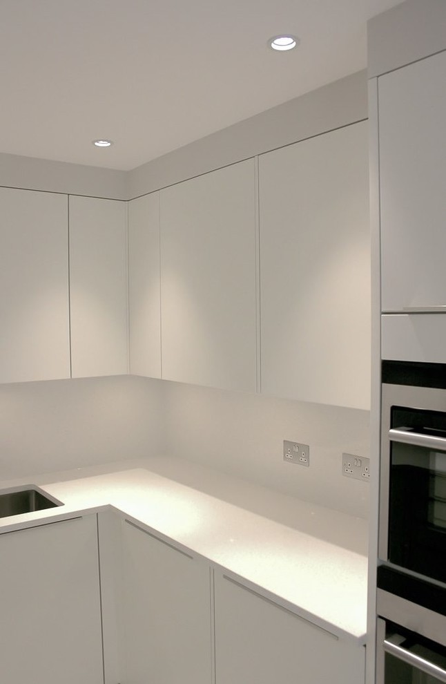 Small contemporary u-shaped separate kitchen in London with a drop-in sink, white cabinets, solid surface benchtops, white splashback, stainless steel appliances and yellow benchtop.