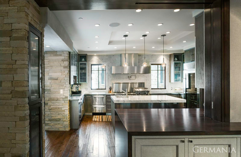 This is an example of an industrial u-shaped enclosed kitchen in Salt Lake City with a built-in sink, flat-panel cabinets, dark wood cabinets, stainless steel worktops, stainless steel appliances, medium hardwood flooring, an island and a drop ceiling.