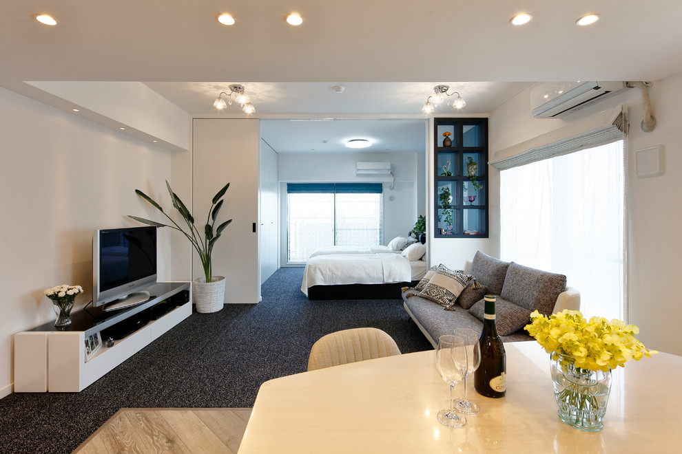 Modern living room in Other with white walls, carpet, a freestanding tv and grey floor.