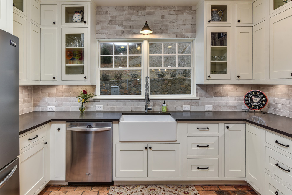 Country u-shaped kitchen in Other with a farmhouse sink, shaker cabinets, white cabinets, beige splashback, brick splashback, stainless steel appliances, brick floors, a peninsula and quartz benchtops.