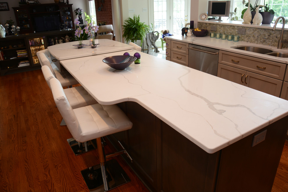This is an example of a large transitional u-shaped open plan kitchen in DC Metro with a double-bowl sink, recessed-panel cabinets, grey cabinets, quartz benchtops, beige splashback, mosaic tile splashback, stainless steel appliances, medium hardwood floors, with island, brown floor and white benchtop.