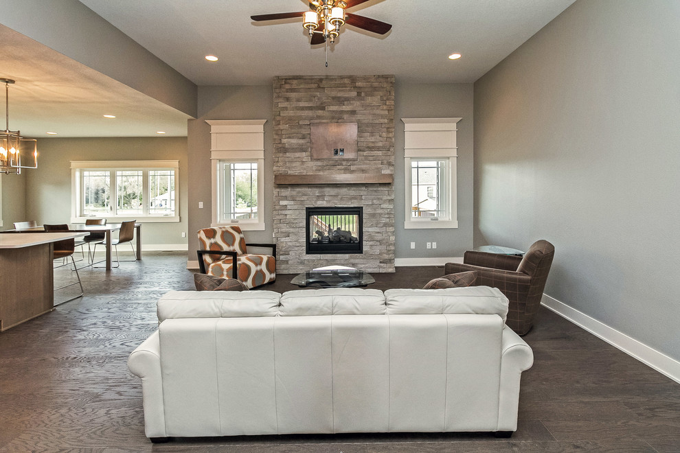 Mid-sized arts and crafts open concept living room in Other with grey walls, medium hardwood floors, a two-sided fireplace, a stone fireplace surround and a wall-mounted tv.