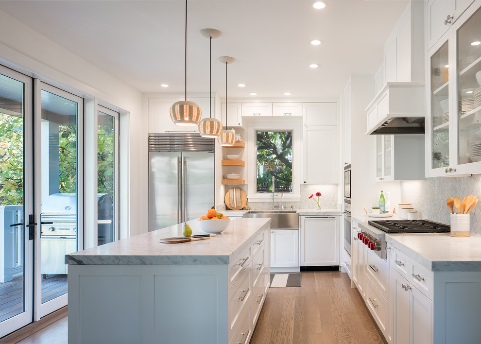 Photo of a transitional l-shaped kitchen in San Francisco with a farmhouse sink, shaker cabinets, white cabinets, grey splashback, stainless steel appliances, medium hardwood floors, with island and brown floor.