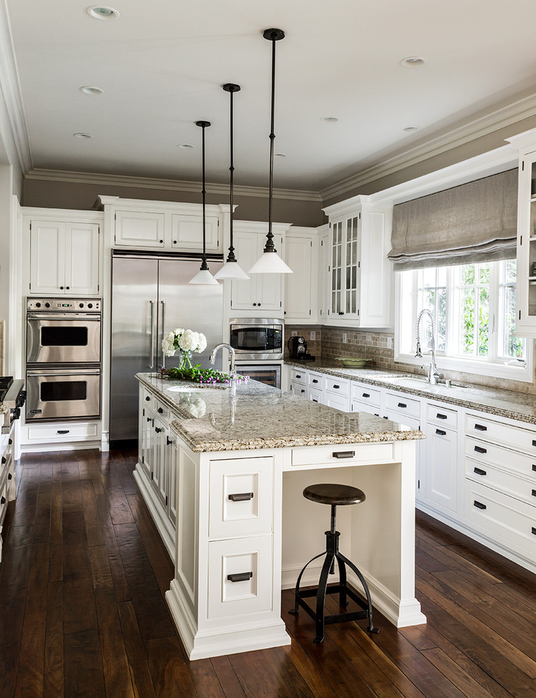 This is an example of a traditional u-shaped kitchen in Los Angeles with recessed-panel cabinets, white cabinets, beige splashback, stainless steel appliances, dark hardwood floors and with island.