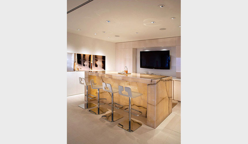 Mid-sized contemporary galley seated home bar in Los Angeles with flat-panel cabinets, light wood cabinets, onyx benchtops, beige splashback, stone slab splashback, ceramic floors and beige floor.
