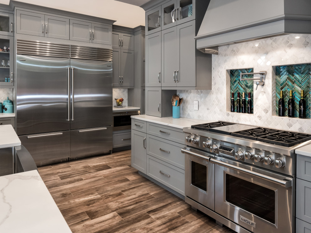 Inspiration for a large transitional l-shaped eat-in kitchen in Miami with a farmhouse sink, shaker cabinets, grey cabinets, quartz benchtops, grey splashback, glass sheet splashback, stainless steel appliances, ceramic floors, with island, brown floor and white benchtop.
