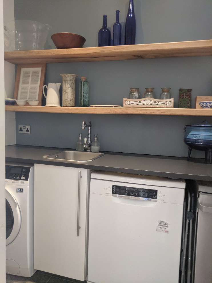 This is an example of a small contemporary single-wall laundry room in London with a single-bowl sink, white cabinets, laminate benchtops, blue splashback, porcelain floors, a side-by-side washer and dryer and grey benchtop.