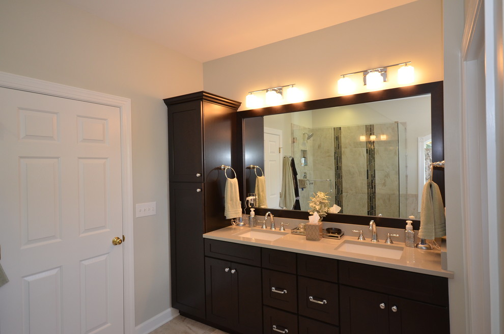 This is an example of a mid-sized traditional master bathroom in Charlotte with an undermount sink, shaker cabinets, brown cabinets, engineered quartz benchtops, a drop-in tub, a two-piece toilet, beige tile, porcelain tile and porcelain floors.