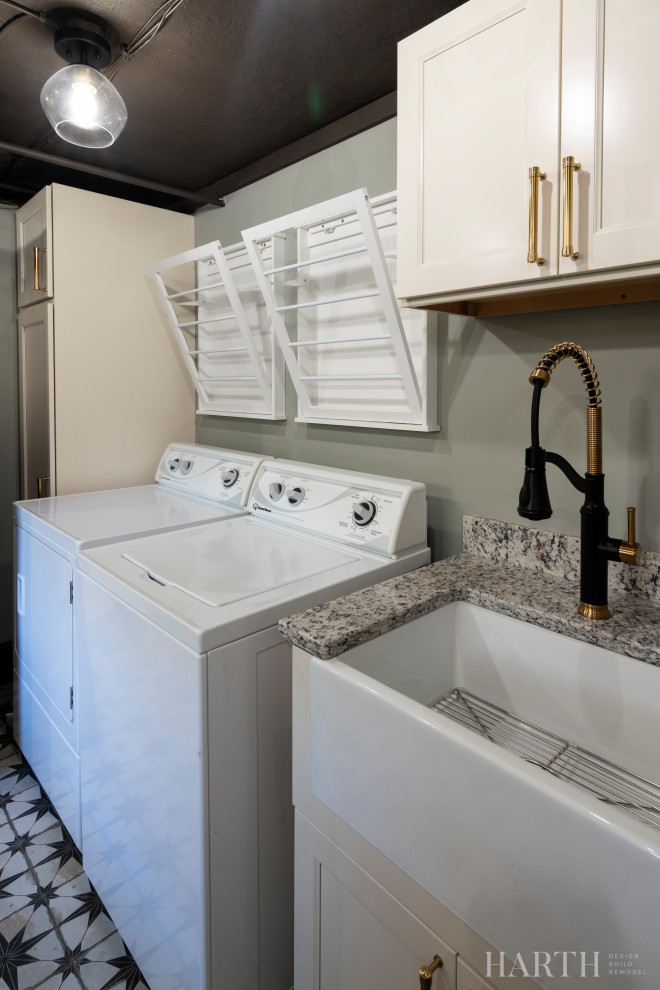 Mid-sized eclectic galley utility room in Philadelphia with a farmhouse sink, recessed-panel cabinets, beige cabinets, granite benchtops, multi-coloured splashback, granite splashback, grey walls, concrete floors, a side-by-side washer and dryer, multi-coloured floor, multi-coloured benchtop and exposed beam.