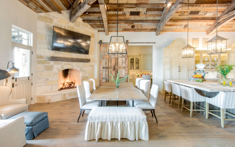 This is an example of a country open plan dining in Austin with white walls, medium hardwood floors, a corner fireplace, a stone fireplace surround and brown floor.