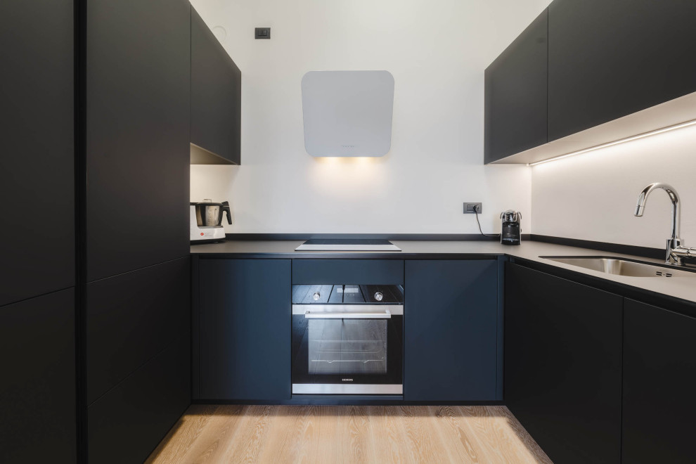 Design ideas for a small contemporary u-shaped kitchen/diner in Milan with a submerged sink, flat-panel cabinets, black cabinets, composite countertops, white splashback, integrated appliances, light hardwood flooring, no island, beige floors and black worktops.