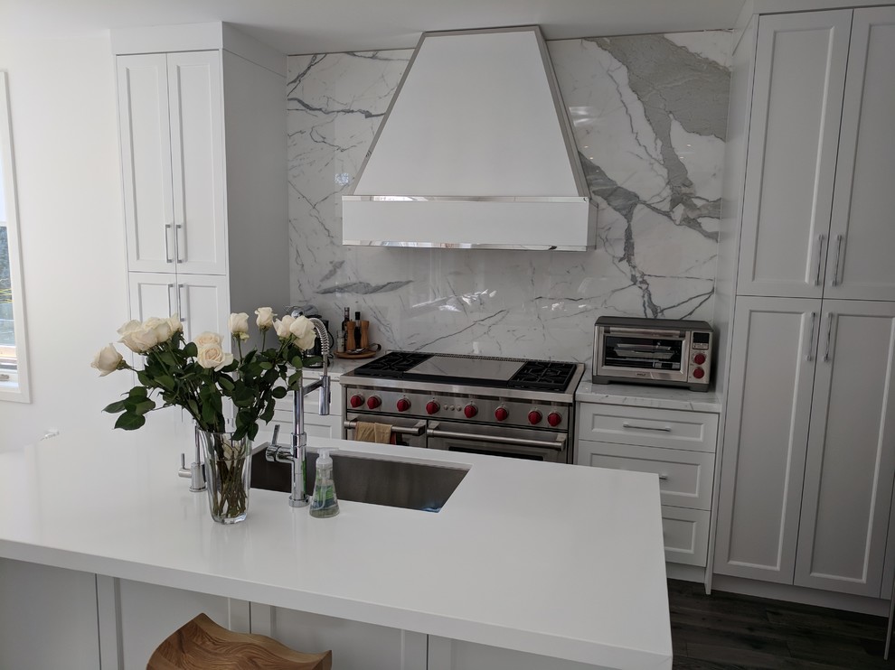 Inspiration for a large contemporary l-shaped open plan kitchen in Toronto with an undermount sink, shaker cabinets, white cabinets, solid surface benchtops, white splashback, marble splashback, panelled appliances, dark hardwood floors, with island and brown floor.