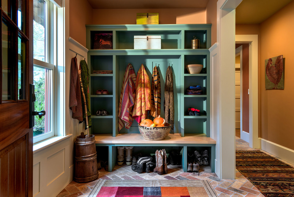 Design ideas for a country mudroom in Burlington with orange walls, brick floors and a dark wood front door.