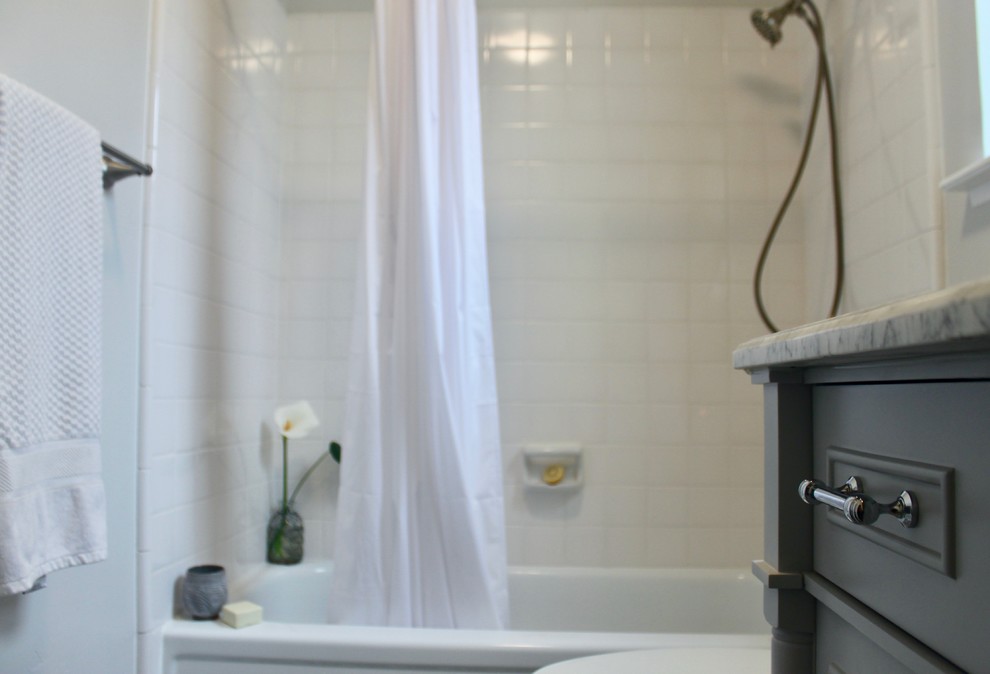 This is an example of a small eclectic bathroom in Sacramento with furniture-like cabinets, grey cabinets, an alcove tub, a shower/bathtub combo, a two-piece toilet, white tile, ceramic tile, grey walls, vinyl floors, an undermount sink, marble benchtops, multi-coloured floor, a shower curtain and grey benchtops.