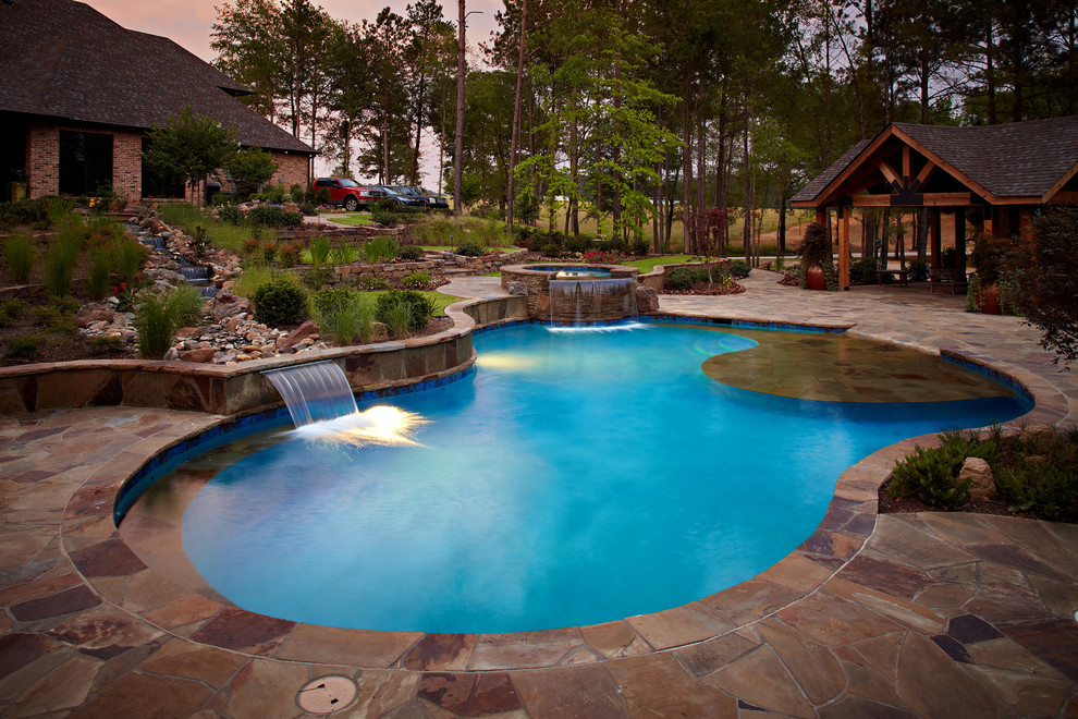 This is an example of a large arts and crafts backyard custom-shaped pool in New Orleans with natural stone pavers and a hot tub.