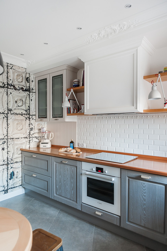Small transitional l-shaped eat-in kitchen in Other with raised-panel cabinets, grey cabinets, wood benchtops, white splashback, subway tile splashback, white appliances, grey floor, brown benchtop, an undermount sink and ceramic floors.