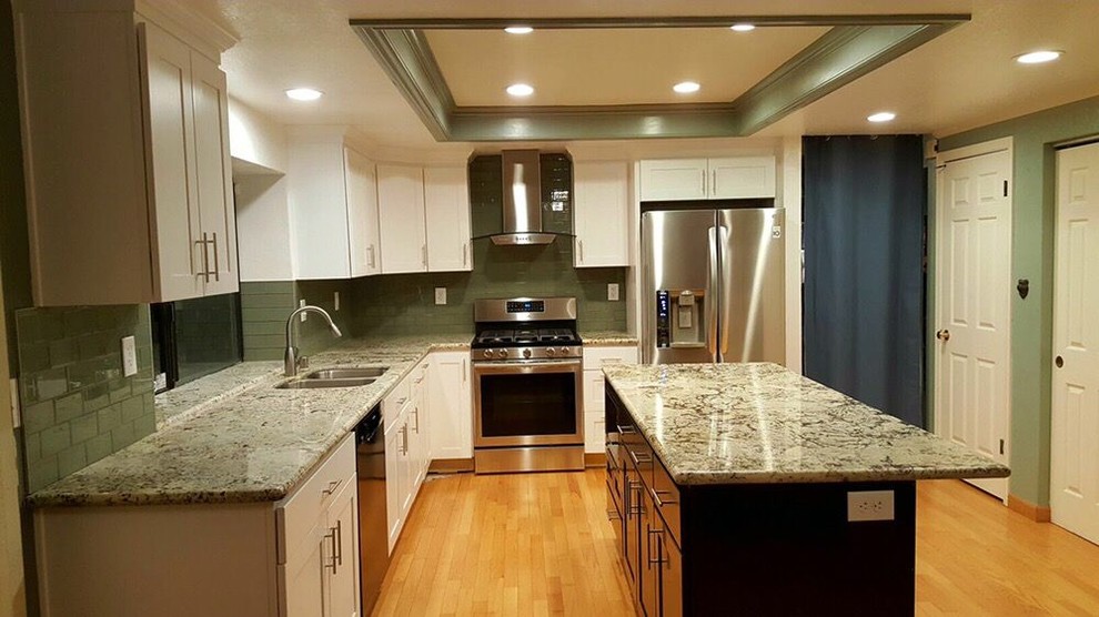 Inspiration for a large transitional l-shaped light wood floor and brown floor enclosed kitchen remodel in San Francisco with a double-bowl sink, shaker cabinets, white cabinets, granite countertops, green backsplash, glass tile backsplash, stainless steel appliances, an island and multicolored countertops