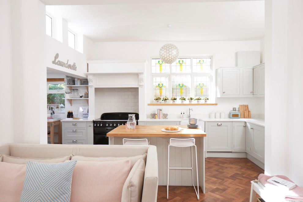 Inspiration for a mid-sized country l-shaped open plan kitchen in London with a farmhouse sink, shaker cabinets, grey cabinets, quartzite benchtops, white splashback, subway tile splashback, a peninsula, brown floor, black appliances and dark hardwood floors.