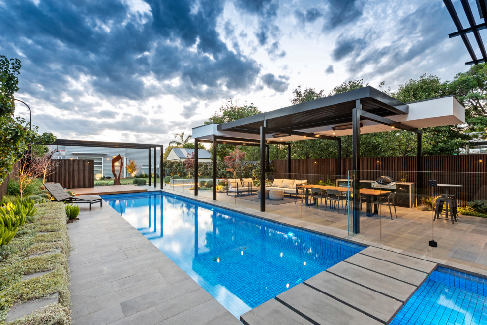 Modelo de casa de la piscina y piscina actual grande rectangular en patio trasero con adoquines de piedra natural