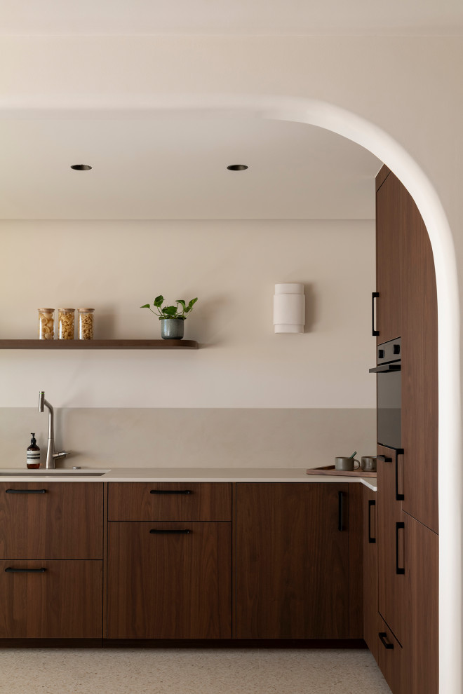 Cette image montre cuisine ouverte en U avec un évier encastré, un placard à porte affleurante, des portes de placard marrons, un plan de travail en quartz modifié, une crédence beige, une crédence en quartz modifié, un sol en terrazzo, aucun îlot, un sol beige et un plan de travail blanc.