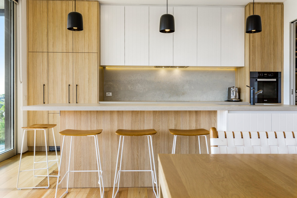 This is an example of a contemporary galley eat-in kitchen in Melbourne with an undermount sink, flat-panel cabinets, medium wood cabinets, grey splashback, black appliances, medium hardwood floors, with island, brown floor and grey benchtop.
