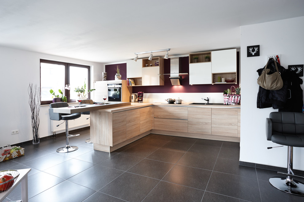 Inspiration for an expansive contemporary single-wall eat-in kitchen in Nuremberg with a drop-in sink, flat-panel cabinets, light wood cabinets, wood benchtops, multi-coloured splashback, black appliances, a peninsula and grey floor.