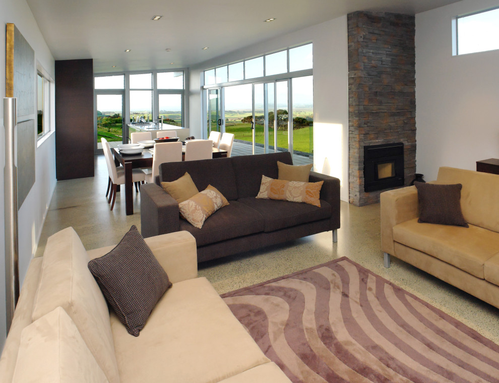 Großes Modernes Wohnzimmer mit weißer Wandfarbe, Betonboden, Kaminofen, Kaminumrandung aus gestapelten Steinen und grauem Boden in Auckland
