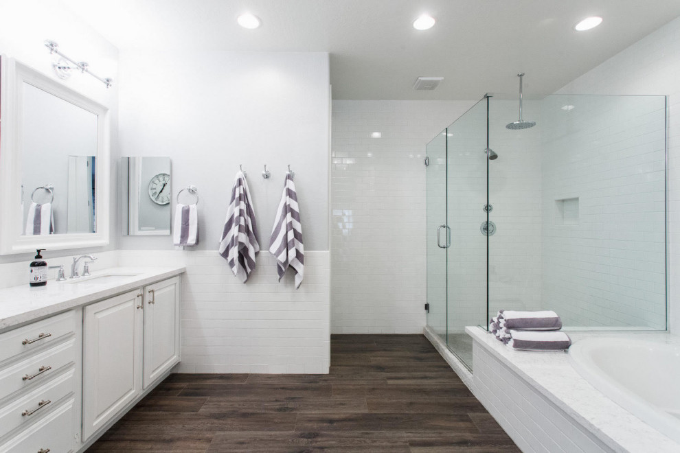 Inspiration for a large transitional master bathroom in Orlando with shaker cabinets, white cabinets, a drop-in tub, a corner shower, white tile, subway tile, grey walls, vinyl floors, an undermount sink, engineered quartz benchtops, brown floor, a hinged shower door and white benchtops.