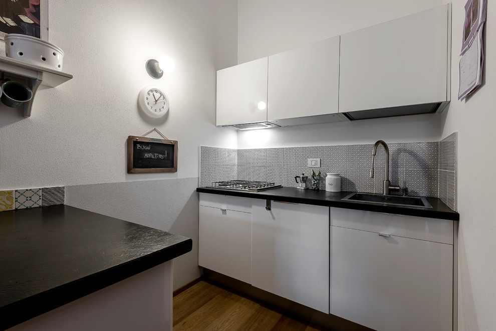 Photo of a contemporary galley kitchen in Milan with a drop-in sink, flat-panel cabinets, white cabinets, stainless steel appliances, light hardwood floors and a peninsula.