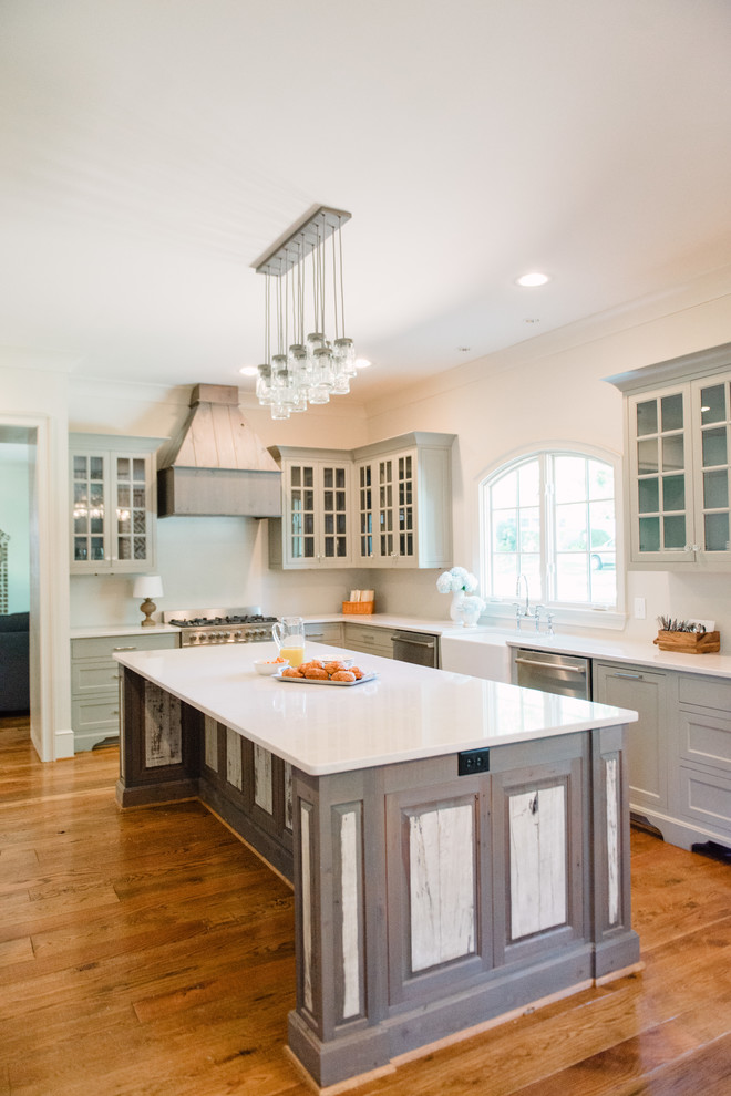 Design ideas for a traditional l-shaped kitchen in Birmingham with a farmhouse sink, glass-front cabinets, blue cabinets, stainless steel appliances, medium hardwood floors and with island.