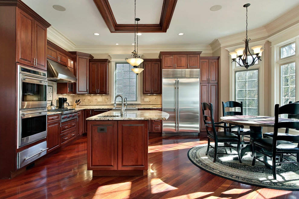 Large traditional l-shaped eat-in kitchen in Los Angeles with an undermount sink, granite benchtops, beige splashback, stainless steel appliances, medium hardwood floors, with island, brown floor, raised-panel cabinets, dark wood cabinets, travertine splashback and multi-coloured benchtop.