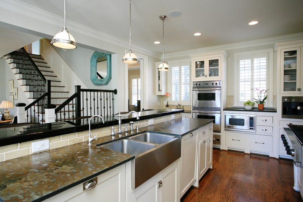 Inspiration for a galley medium tone wood floor kitchen pantry remodel in Raleigh with a farmhouse sink, raised-panel cabinets, white cabinets, granite countertops, white backsplash, cement tile backsplash, stainless steel appliances and an island