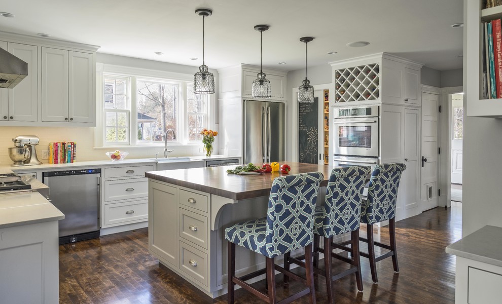 Mid-sized country l-shaped eat-in kitchen in Boston with a farmhouse sink, shaker cabinets, white cabinets, quartz benchtops, white splashback, porcelain splashback, stainless steel appliances, dark hardwood floors and with island.