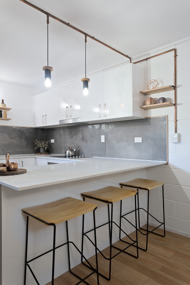 Inspiration for a mid-sized industrial u-shaped eat-in kitchen in Gold Coast - Tweed with a drop-in sink, flat-panel cabinets, white cabinets, quartz benchtops, grey splashback, porcelain splashback, stainless steel appliances and white benchtop.