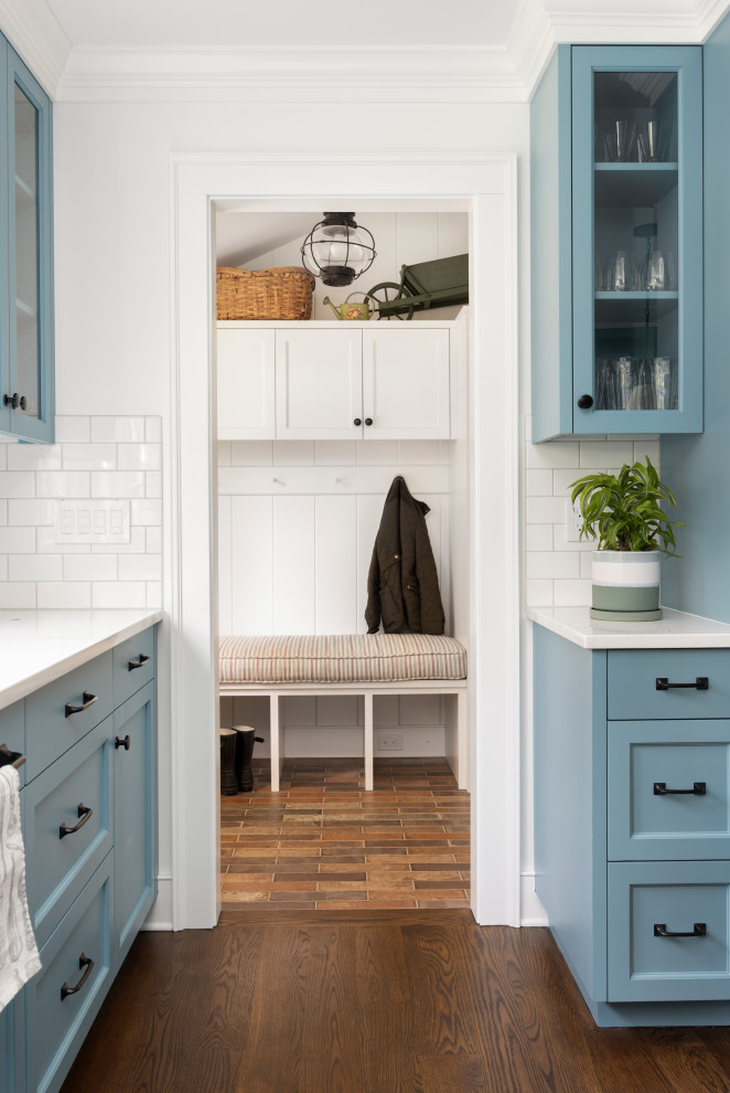 Klassisk inredning av ett mycket stort vit vitt kök, med en undermonterad diskho, luckor med profilerade fronter, blå skåp, bänkskiva i kvarts, vitt stänkskydd, stänkskydd i keramik, rostfria vitvaror, mellanmörkt trägolv och en köksö