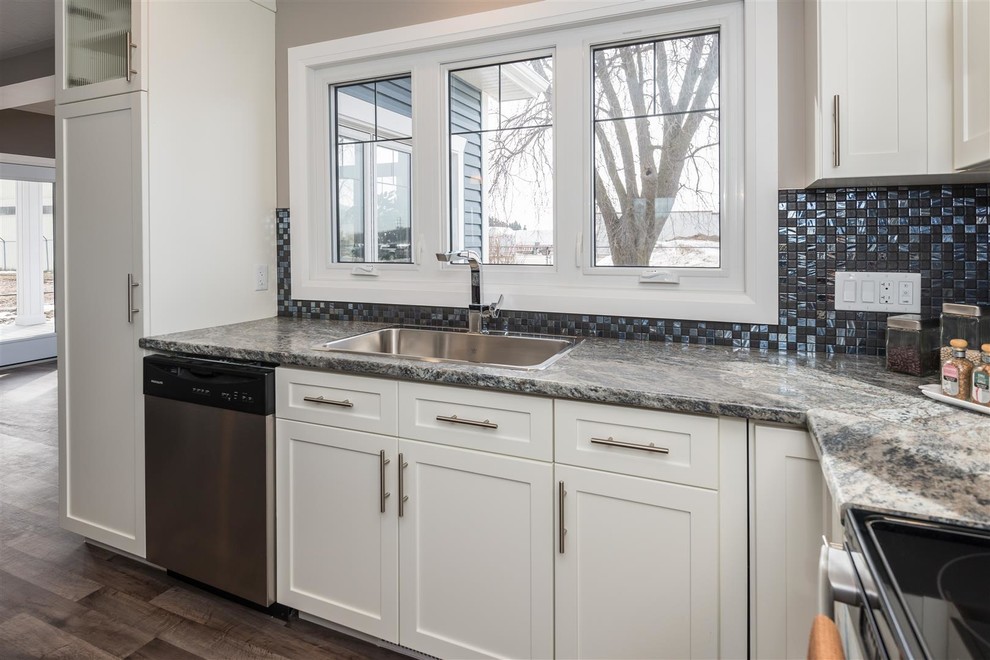 Example of a mid-sized transitional l-shaped medium tone wood floor and brown floor eat-in kitchen design with a drop-in sink, shaker cabinets, white cabinets, granite countertops, metallic backsplash, mosaic tile backsplash, stainless steel appliances, an island and multicolored countertops