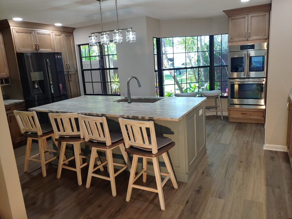 This is an example of a large u-shaped open plan kitchen in Tampa with a submerged sink, recessed-panel cabinets, distressed cabinets, quartz worktops, green splashback, glass tiled splashback, stainless steel appliances, vinyl flooring, an island, brown floors and brown worktops.