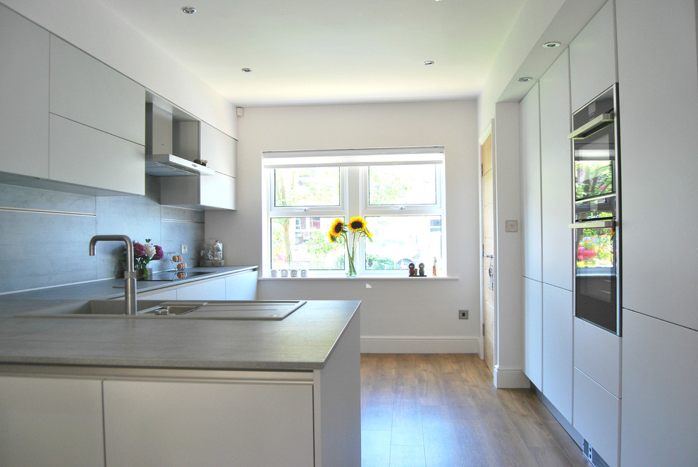 This is an example of a mid-sized contemporary eat-in kitchen in Buckinghamshire with flat-panel cabinets, grey cabinets, laminate benchtops, grey splashback and a peninsula.