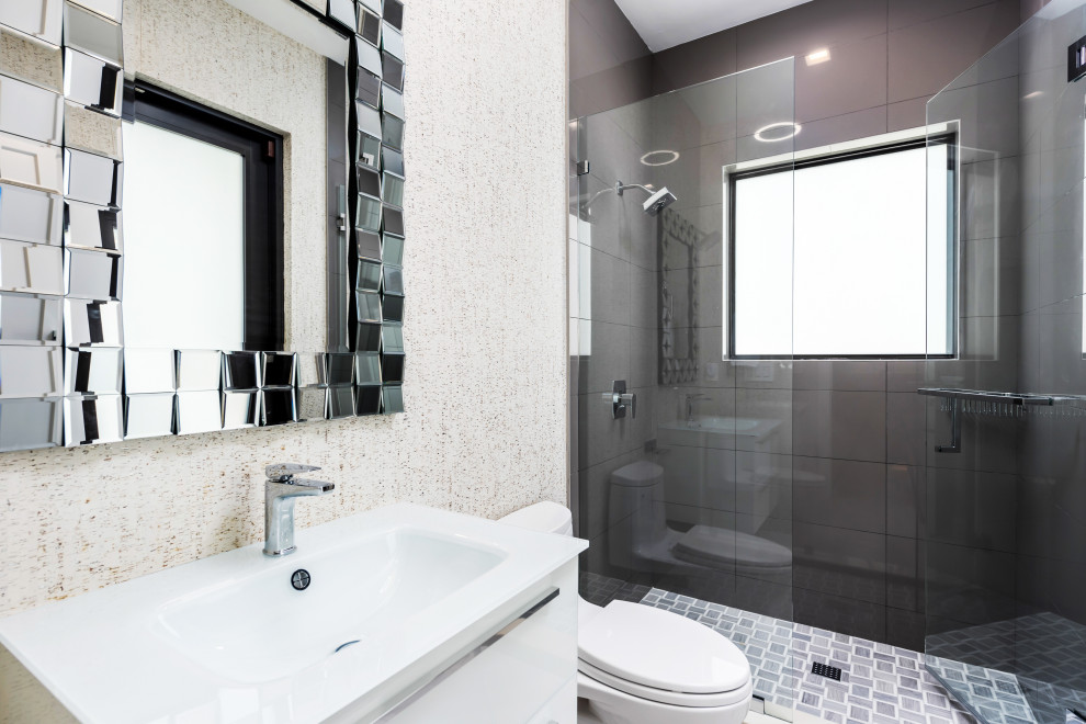 Mid-sized contemporary bathroom in Miami with flat-panel cabinets, white cabinets, a curbless shower, a one-piece toilet, gray tile, glass sheet wall, beige walls, marble floors, an integrated sink, quartzite benchtops, grey floor, a hinged shower door, white benchtops, a single vanity, a freestanding vanity and wallpaper.