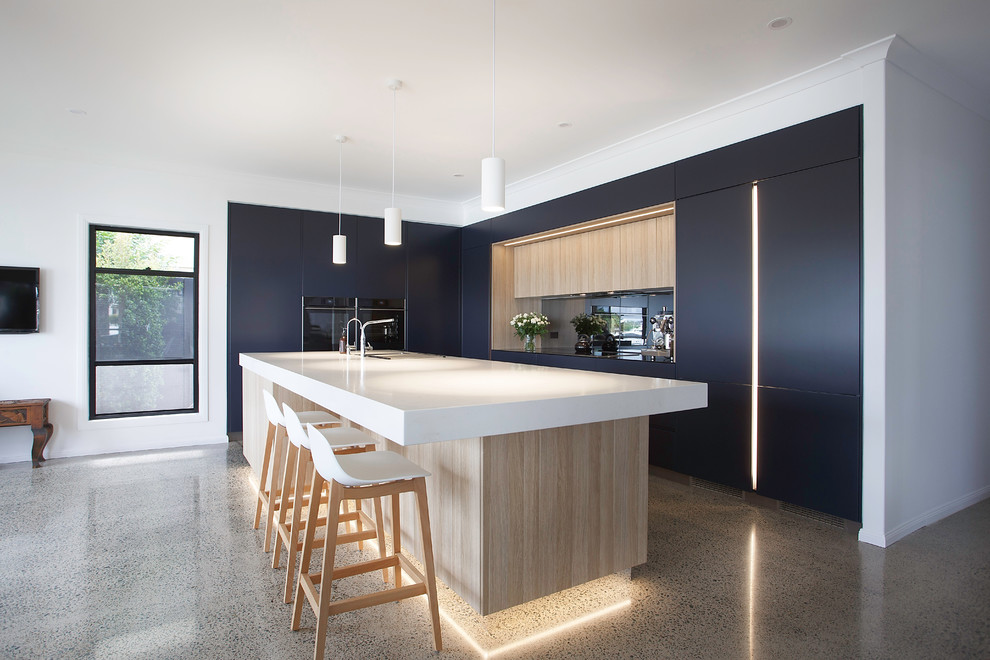 Photo of a large contemporary l-shaped open plan kitchen in Brisbane with a double-bowl sink, flat-panel cabinets, quartz benchtops, mirror splashback, black appliances, concrete floors, with island, white benchtop, black cabinets and grey floor.