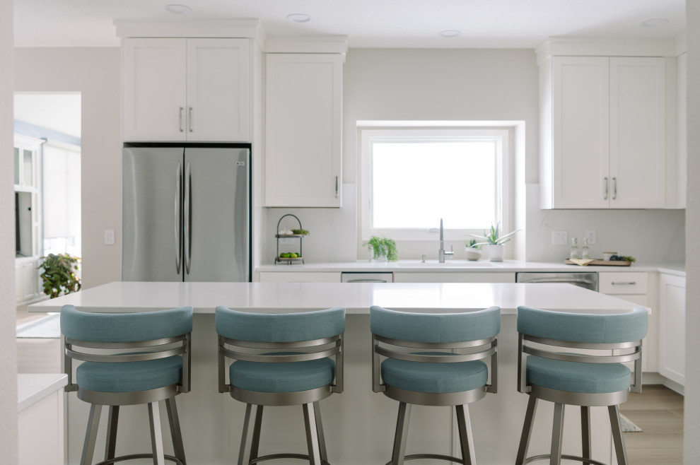 Inspiration for a large transitional l-shaped laminate floor and brown floor eat-in kitchen remodel with an undermount sink, shaker cabinets, white cabinets, quartz countertops, white backsplash, quartz backsplash, stainless steel appliances, an island and white countertops