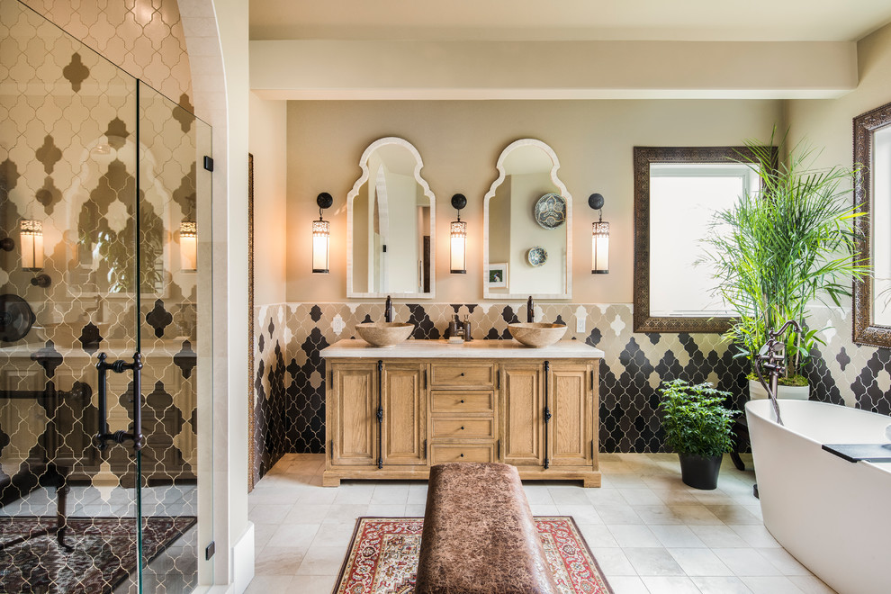 Design ideas for a mediterranean master bathroom in Seattle with light wood cabinets, a freestanding tub, ceramic tile, beige walls, ceramic floors, a vessel sink, marble benchtops, a hinged shower door, an alcove shower, beige tile, brown tile, gray tile, white tile, beige floor and recessed-panel cabinets.