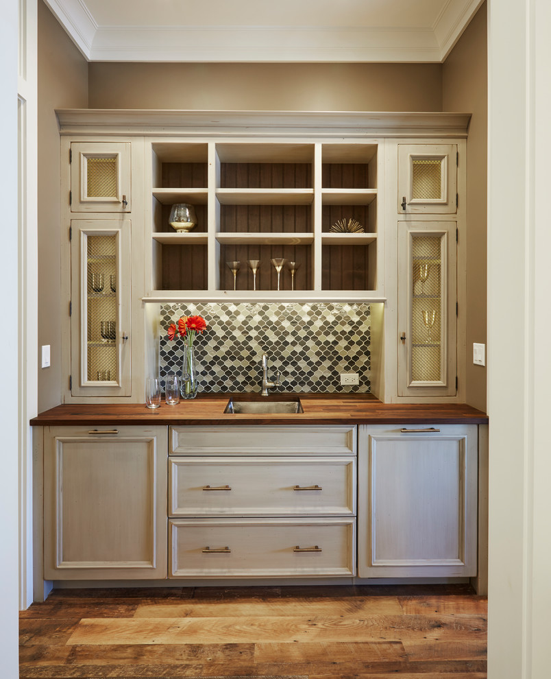 Photo of a small transitional single-wall wet bar in Chicago with an undermount sink, flat-panel cabinets, beige cabinets, wood benchtops, green splashback, medium hardwood floors, brown floor and brown benchtop.