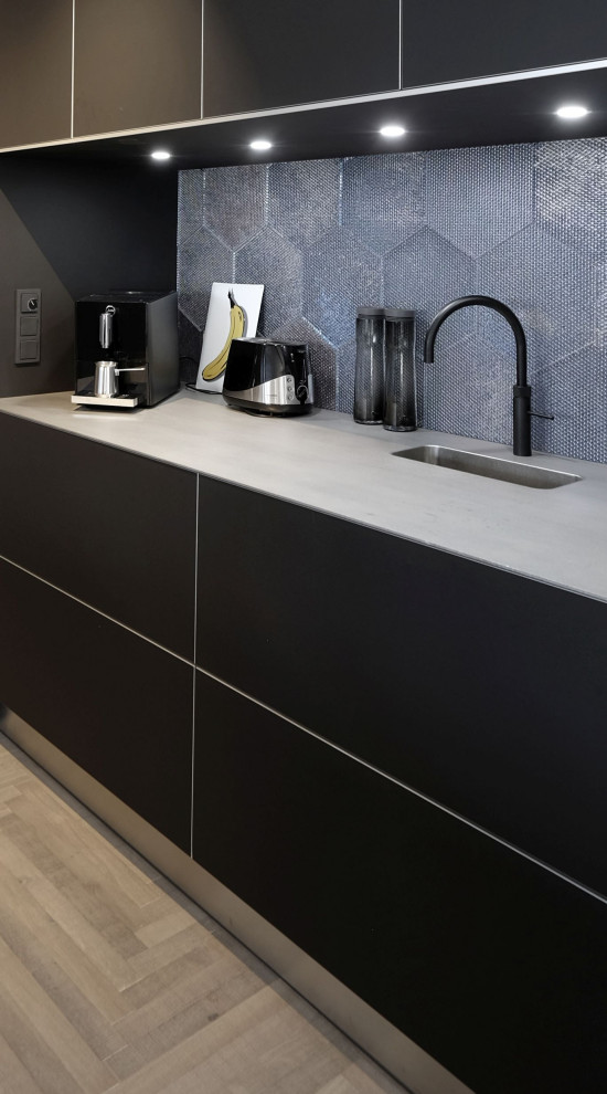Inspiration for an expansive industrial galley open plan kitchen in Cologne with an integrated sink, flat-panel cabinets, black cabinets, stainless steel benchtops, black appliances, with island and grey floor.