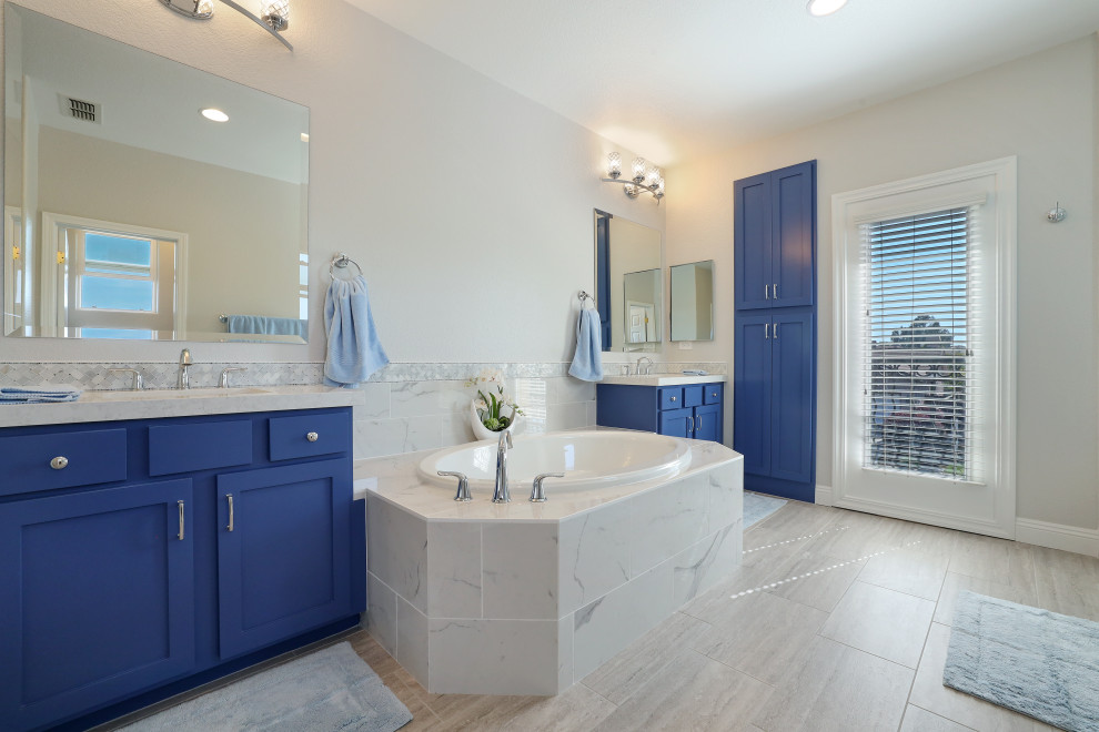 Cette image montre une salle de bain principale minimaliste avec des portes de placard bleues, une baignoire posée, une douche d'angle, un carrelage blanc, des carreaux de porcelaine, un mur blanc, un sol en carrelage de porcelaine, un lavabo encastré, un sol beige, une cabine de douche à porte battante, un plan de toilette blanc, meuble double vasque et meuble-lavabo encastré.