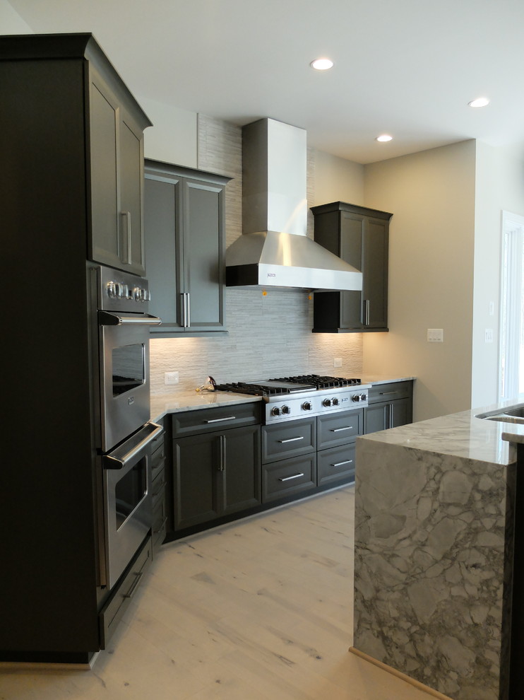 Large transitional kitchen in DC Metro with a double-bowl sink, dark wood cabinets, stainless steel appliances, light hardwood floors, with island, raised-panel cabinets, granite benchtops, grey splashback and stone tile splashback.