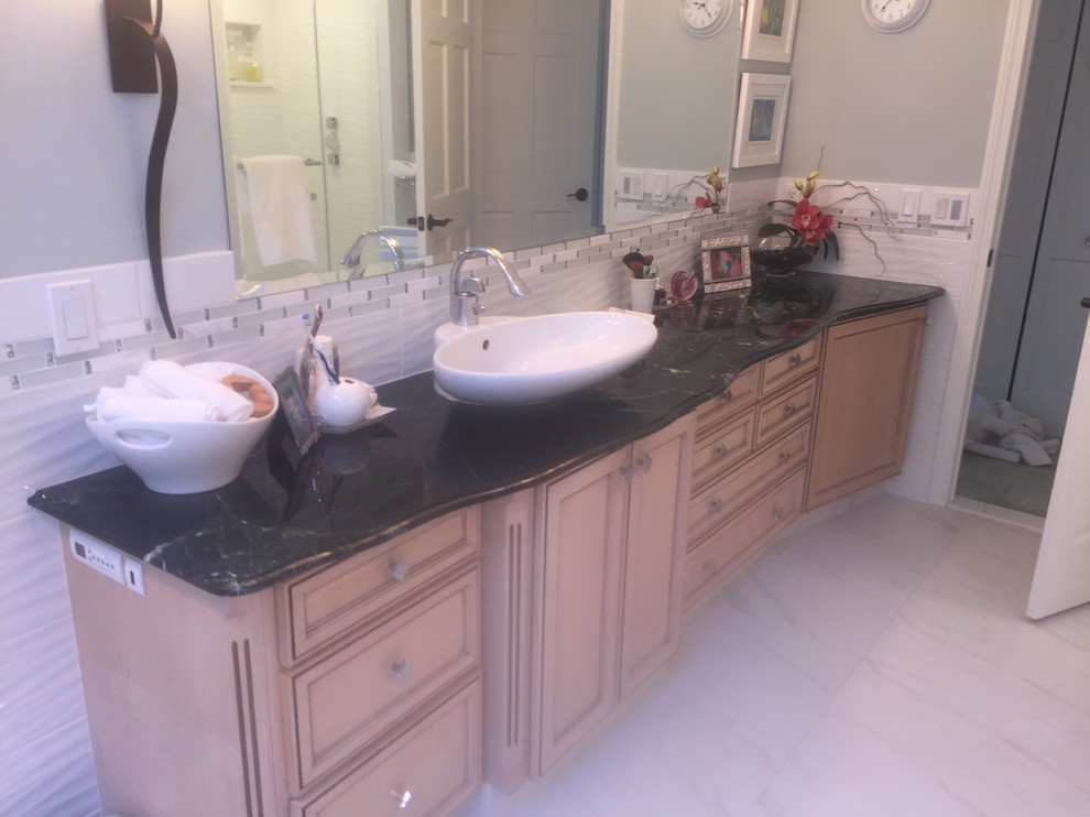 Mid-sized transitional master bathroom in Providence with recessed-panel cabinets, light wood cabinets, a freestanding tub, an alcove shower, white tile, porcelain tile, grey walls, marble floors, a vessel sink, soapstone benchtops, grey floor, a hinged shower door and black benchtops.