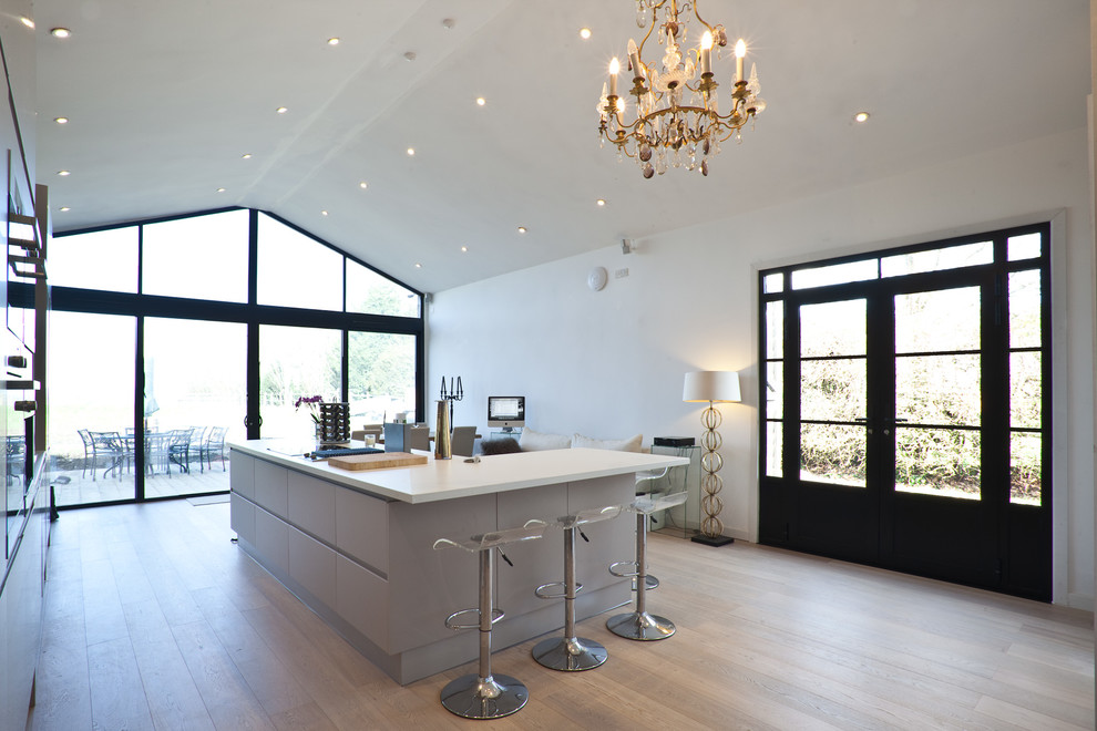 This is an example of a contemporary kitchen/diner in London with a single-bowl sink, flat-panel cabinets, beige cabinets, mirror splashback, stainless steel appliances, light hardwood flooring and an island.