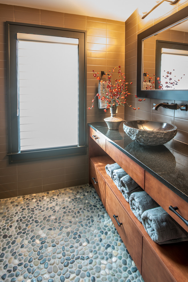 Inspiration for a large transitional master beige tile, brown tile, gray tile and ceramic tile pebble tile floor bathroom remodel with flat-panel cabinets, medium tone wood cabinets, brown walls, a vessel sink and quartzite countertops