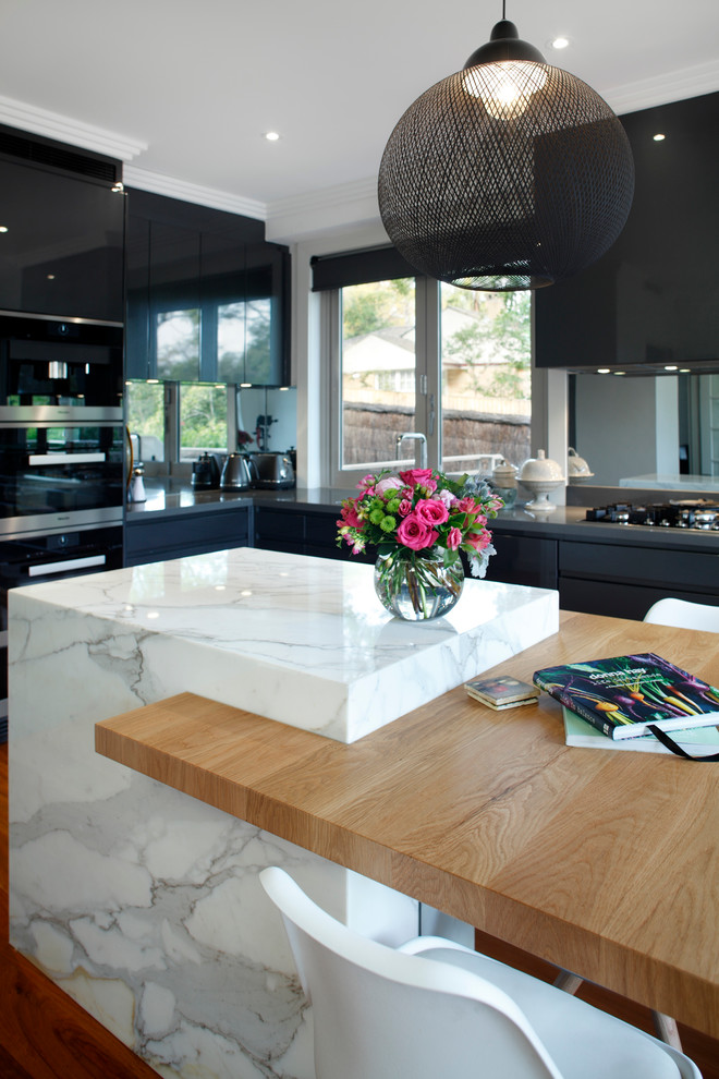 Photo of a mid-sized contemporary l-shaped eat-in kitchen in Sydney with an undermount sink, recessed-panel cabinets, grey cabinets, marble benchtops, metallic splashback, mirror splashback, black appliances, light hardwood floors and with island.